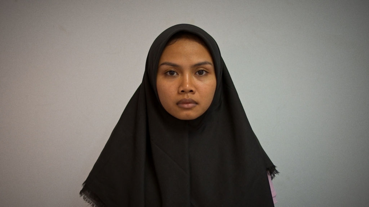 A young woman wearing a headscarf stares at the camera.